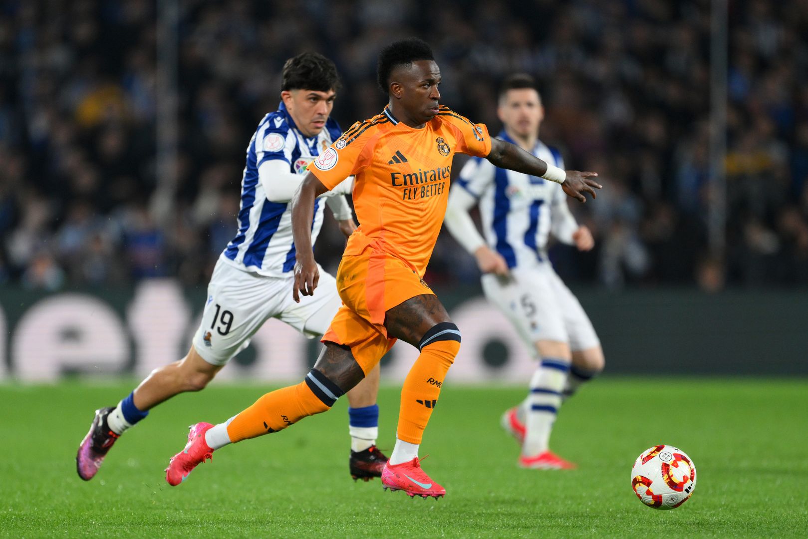 SAN SEBASTIAN, SPAIN - FEBRUARY 26: Vinicius Junior of Real Madrid runs with the ball whilst under pressure from Jon Aramburu of Real Sociedad during the Copa del Rey Semi Final match between Real Sociedad and Real Madrid at Reale Arena on February 26, 2025 in San Sebastian, Spain.