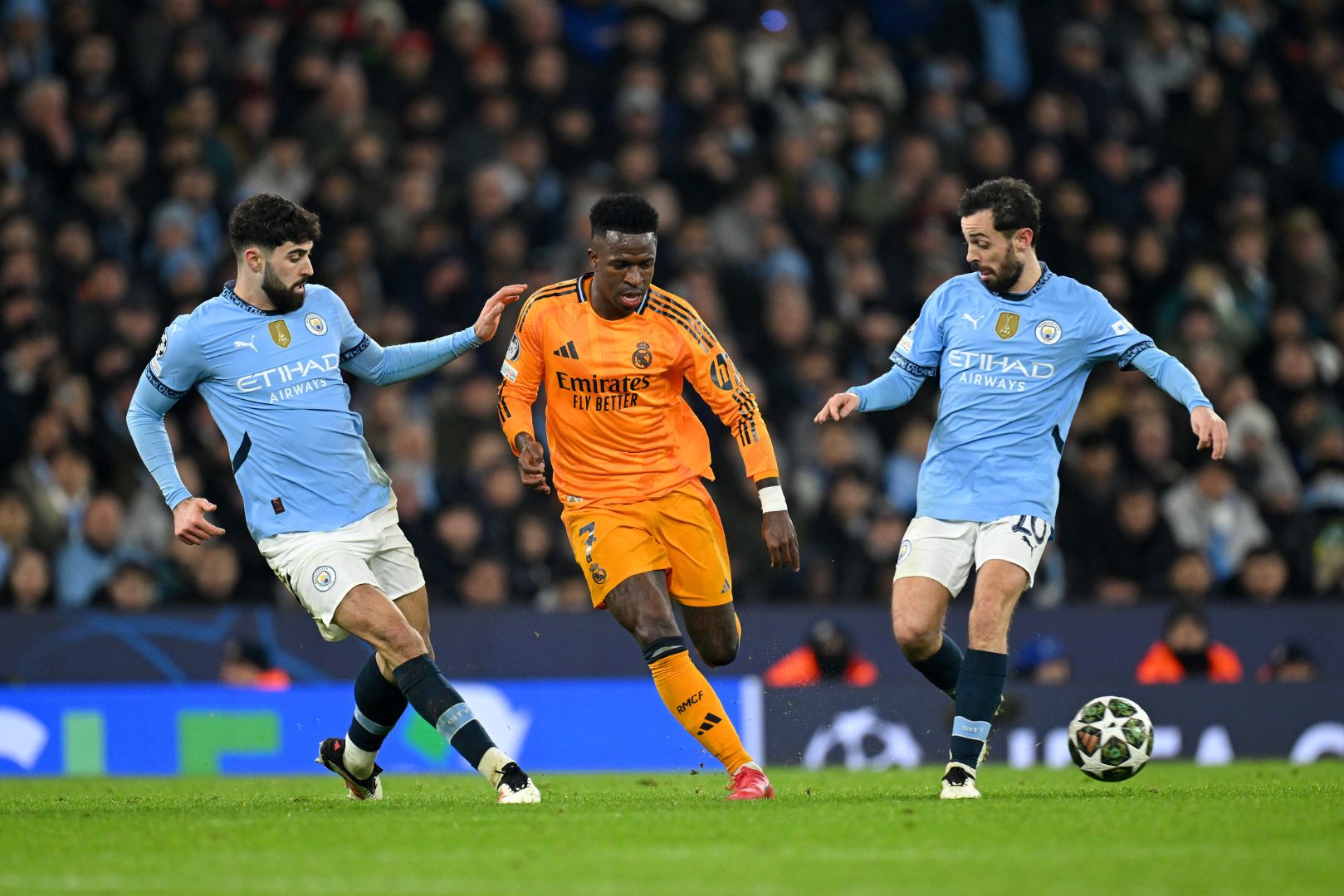 MANCHESTER, ENGLAND - FEBRUARY 11: Vinicius Junior of Real Madrid makes a pass whilst under pressure from Josko Gvardiol and Bernardo Silva of Manchester City during the UEFA Champions League 2024/25 League Knockout Play-off first leg match between Manchester City and Real Madrid C.F. at Manchester City Stadium on February 11, 2025 in Manchester, England.